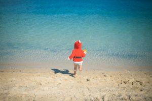 child wearing santa costume at the beach during a sunny day