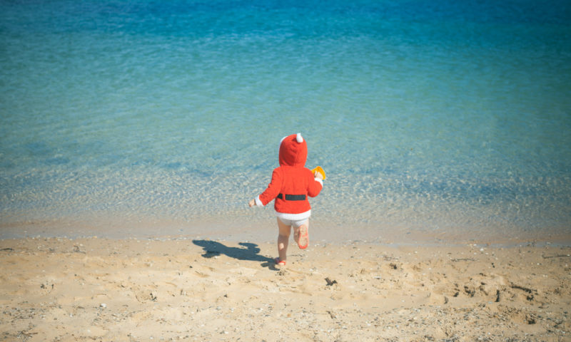 child wearing santa costume at the beach during a sunny day