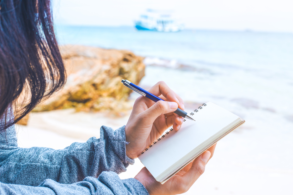 woman writing down her thoughts on a journal at the beach 